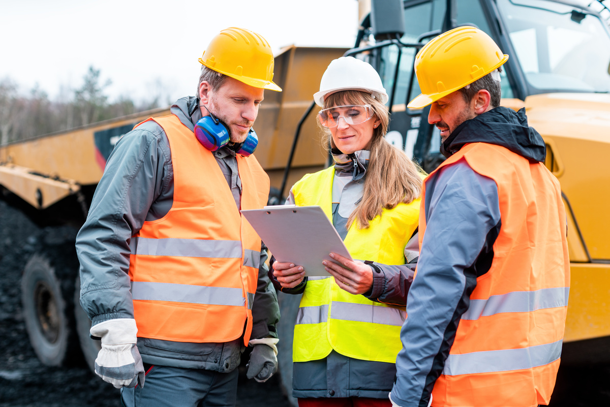 Three Workers in Quarry Discussing in Front of Heavy Machinery